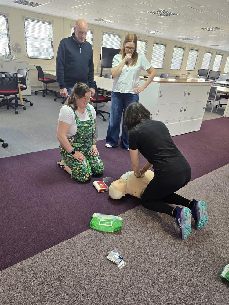 Trainee performing CPR on a manikin while colleagues observe during workplace first aid training